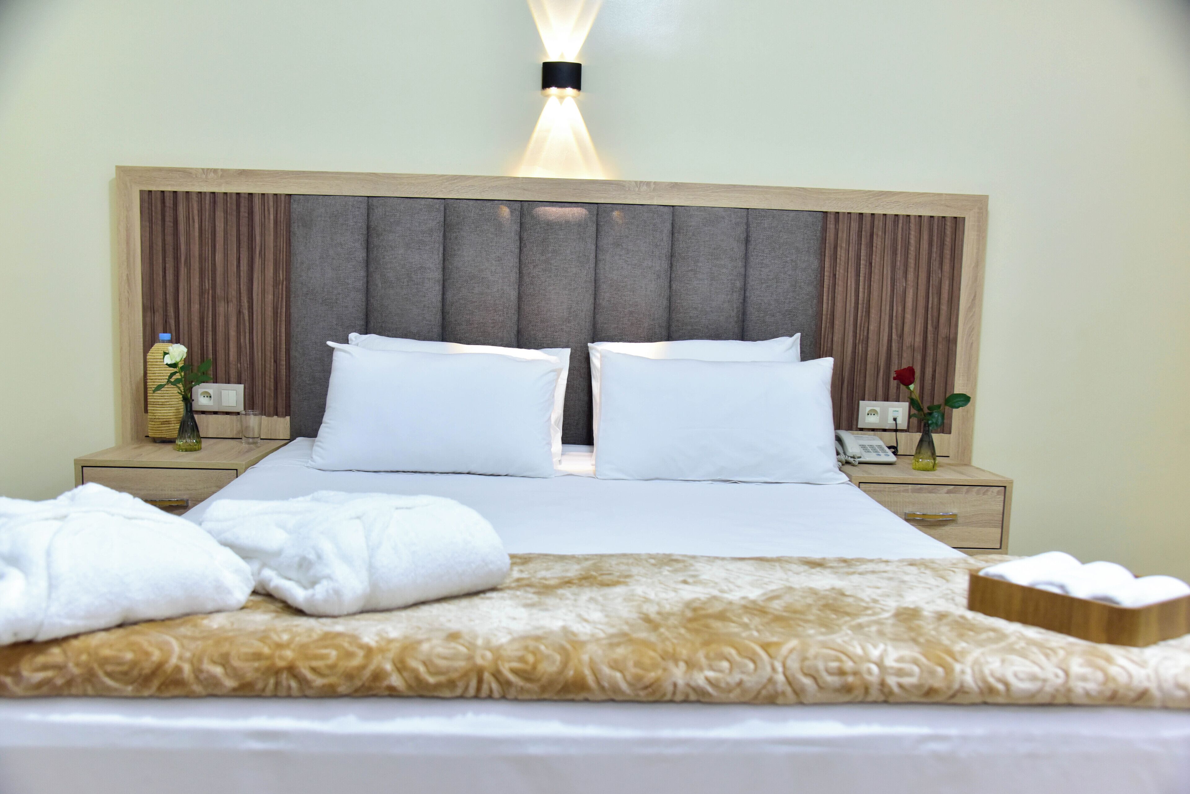 A hotel room with a large bed, two bedside tables, a nightstand, a lamp, and a vase with a flower.