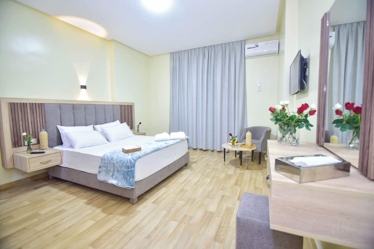 Quarto de hotel com cama, mesa de cabeceira, abajur, cadeira e uma pequena mesa com flores.