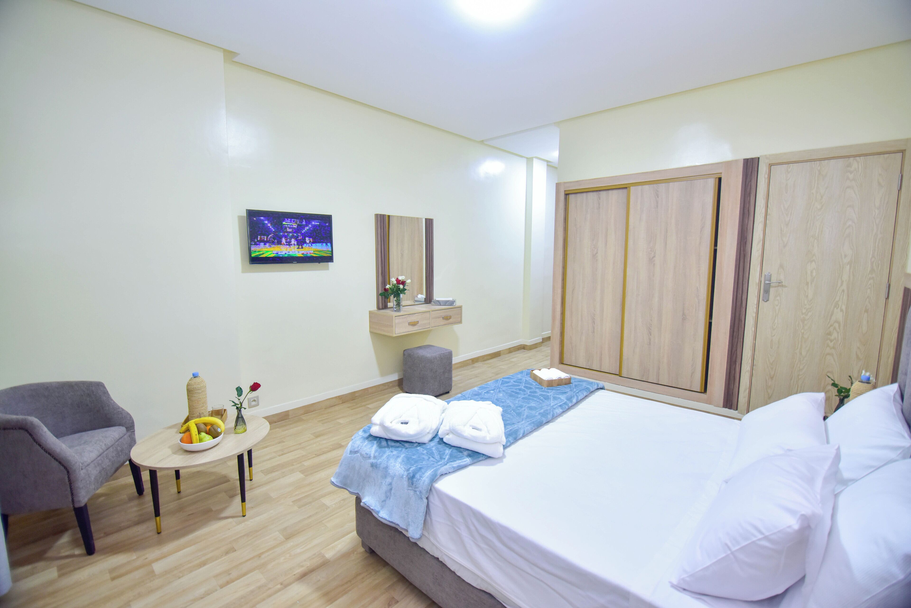 Habitación de hotel con cama, una silla, una mesita con frutero, televisión y armario.
