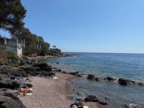 A rocky beach with clear water, a few people sunbathing, and a building with a balcony overlooking the sea. - Luxury bungalow - Sea view - Heated pool 4 (Saint-Raphaël)