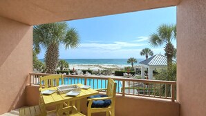 A balcony with a yellow table and chairs, overlooking a beach with palm trees and a clear sky. - Beach Club D209- Direct Gulf View - Beach - Pool - WIFI (Gulf Shores)