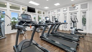A gym with multiple treadmills, exercise bikes, and a television screen displaying workout videos. - Beach Club D209- Direct Gulf View - Beach - Pool - WIFI (Gulf Shores)