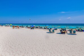 Una spiaggia con file di lettini e ombrelloni, cielo sereno e l'oceano sullo sfondo.