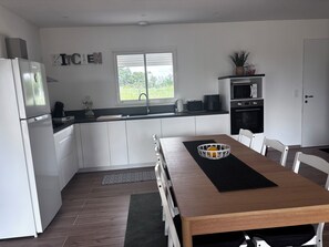 Une cuisine moderne avec des meubles blancs, une table à manger en bois et une fenêtre donnant sur un paysage verdoyant.