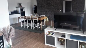 Un salón moderno con televisor, mesa de comedor, sillas y una cocina al fondo.