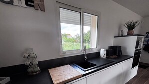 Una cocina moderna con cubierta negra, armarios blancos, una ventana con persianas, una cafetera y una planta en la encimera.