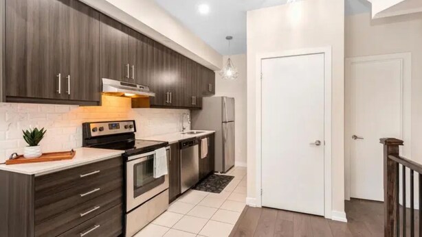 Una cocina moderna con alacenas de madera oscura, electrodomésticos de acero inoxidable y una puerta blanca.