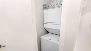 Un lavadero pequeño y blanco con lavadora y secadora apiladas, una puerta y un panel de control en la pared.