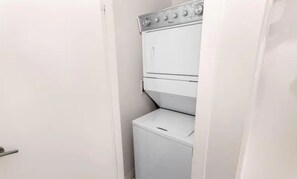 Ein kleiner, weißer Hauswirtschaftsraum mit nebeneinander gestapelten Waschmaschine und Trockner, einer Tür und einer an der Wand montierten Steuerung.