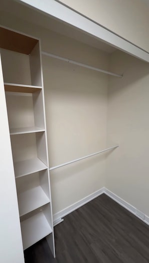 Ein begehbarer Kleiderschrank mit weißen Regalen und Holzboden.