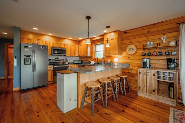 Una cocina con gabinetes de madera, un refrigerador de acero inoxidable, un microondas, un lavamanos y taburetes de bar.