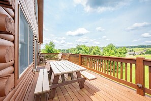 A wooden deck with a picnic table and chairs, overlooking a green landscape. - New! Lake Access Home w/ Hot Tub! (Swanton)