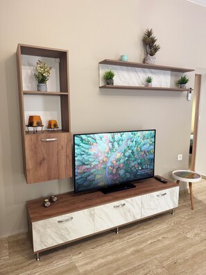 A modern living room with a TV on a wooden cabinet, a marble side table, and shelves with plants and decorative items. - Modern cozy home in Kos town (Kos)