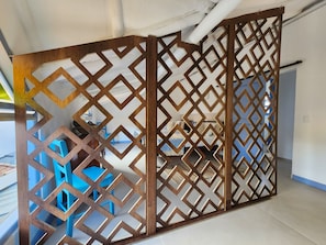 Ein Zimmer mit einer Holzwand mit geometrischen Ausschnitten, einem blauen Sessel und einem Bett mit weißer Bettwäsche.