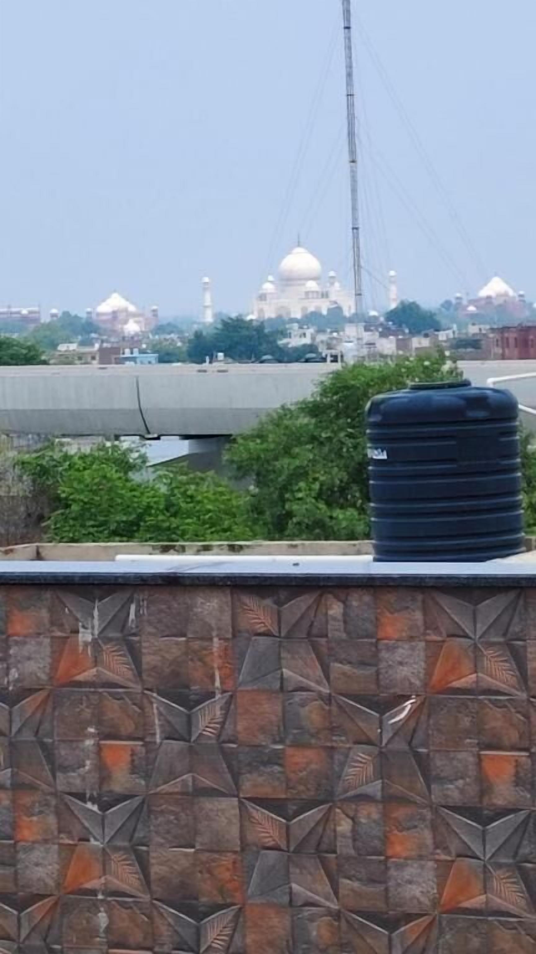 A tiled wall with a water tank and a view of a large white building with domes.