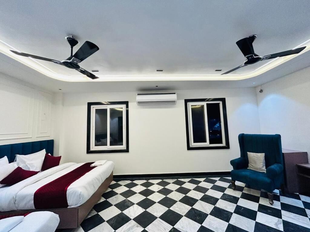A hotel room with a checkered floor, two beds, a blue armchair, and ceiling fans.