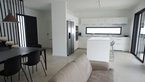 Une cuisine moderne avec des meubles blancs, un îlot central et un coin repas comprenant une table et des chaises.