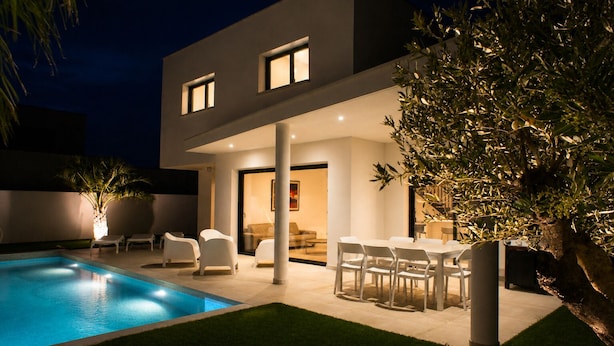 Une maison moderne à deux étages, dotée d’une piscine, d’un espace extérieur aménagé et d’un intérieur bien éclairé.