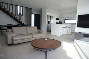Un salon moderne comprenant un canapé, une table basse, un escalier et un coin cuisine.
