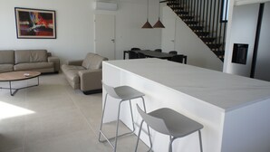 Une cuisine moderne dotée d’un îlot central, de tabourets de bar, d’un coin repas avec une table et des chaises, d’un escalier et d’un salon avec un canapé et une table basse.