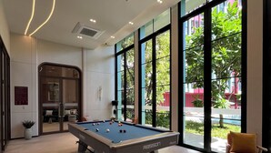 Una mesa de billar en una habitación moderna con ventanas amplias, una silla y una puerta que da a otra zona.