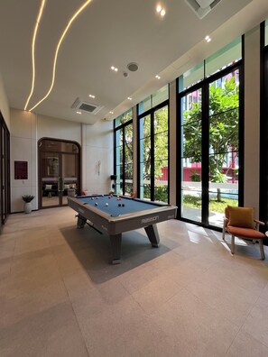 A pool table in a modern room with large windows, a chair, and a door leading to another area. - Monthly, 1 bedroom in cozy The Base condo near Central Phuket (Tambon Wichit)