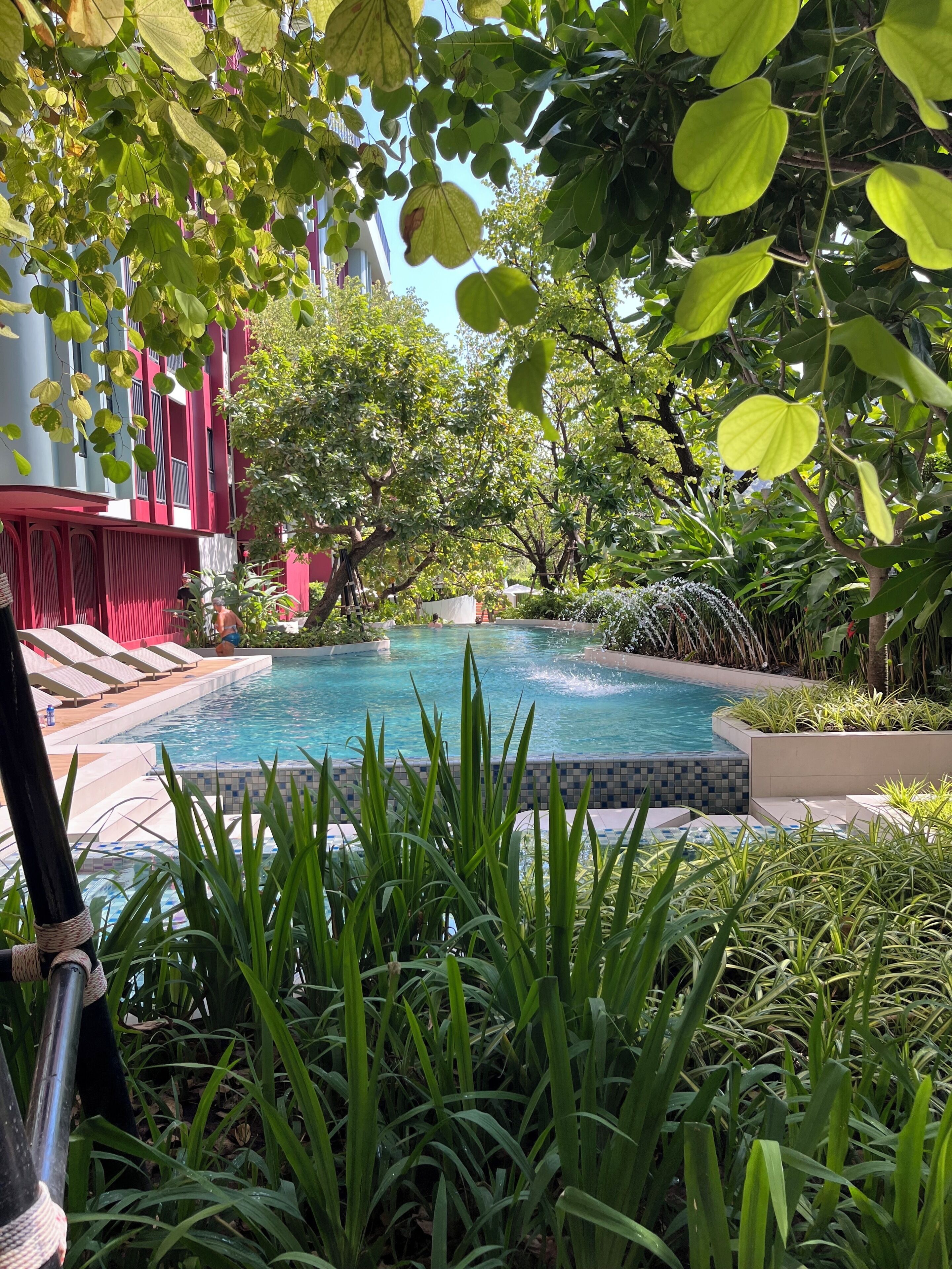 Piscina rodeada por vegetação exuberante e um edifício vermelho.