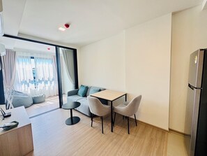 A modern hotel room with a sofa, two chairs, a small table, a desk, and a refrigerator. - Monthly, 1 bedroom in cozy The Base condo near Central Phuket (Tambon Wichit)
