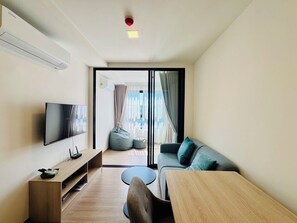 A modern living room with a flat-screen TV, a wooden coffee table, a sofa, and a small round table. - Monthly, 1 bedroom in cozy The Base condo near Central Phuket (Tambon Wichit)