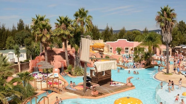 A large outdoor swimming pool with multiple water features, palm trees, and a rocky landscape. - Holiday Park Stay With Sun, Slides & Sea (Hyères)