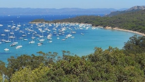 A coastal area with numerous boats anchored in clear blue waters, surrounded by dense green vegetation and distant mountains. - Holiday Park Stay With Sun, Slides & Sea (Hyères)