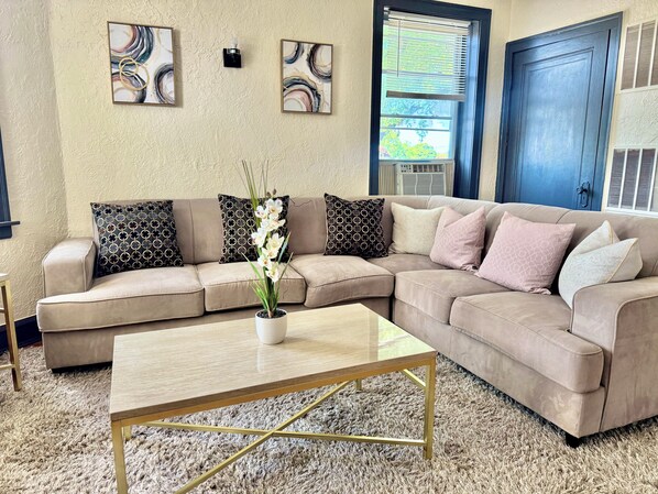 A living room with a beige sectional sofa, a wooden coffee table, and a decorative orchid plant.