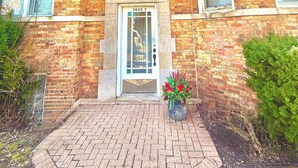 Un bâtiment en briques doté d’une entrée centrale, de nombreuses fenêtres et d’un petit jardin agrémenté de fleurs.