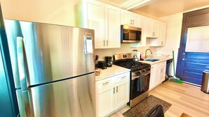 Une cuisine de taille réduite avec des meubles blancs, un réfrigérateur en acier inoxydable, un four à micro-ondes, une cuisinière et un évier.