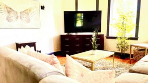 Un salon comprenant un canapé, une table basse, un téléviseur, un meuble en bois foncé et une plante en pot.