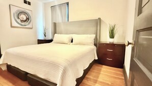 Une chambre avec un grand lit, une table de chevet, une plante en pot et une fenêtre avec des rideaux.