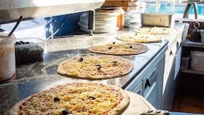 A kitchen with multiple pizza ovens, pizza toppings, and pizza boxes. - Family Lodge Near Beach & Pool (Hyères)