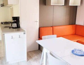 A compact kitchen with a coffee maker, a small refrigerator, and a white table with a blue object on it. - Family Lodge Near Beach & Pool (Hyères)