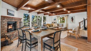 Ein gemütliches Wohnzimmer mit Kamin, Holzbalkendecke, einem Essbereich mit Tisch und Stühlen sowie einer Couch.
