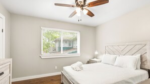 A bedroom with a bed, a ceiling fan, a window with blinds, a bedside table with a lamp, and a dresser. - Glendale Court Unit 6 (Dallas)