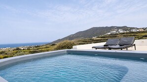 A swimming pool with lounge chairs, a clear view of the sea, and a hillside in the background. - Zen Villas Oia  (Oia)