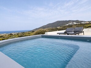 A swimming pool with lounge chairs, a clear view of the sea, and a hillside in the background. - Zen Villas Oia  (Oia)