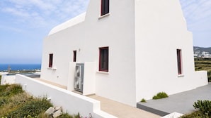 A white building with a flat roof, a small door, and two windows with red frames. - Zen Villas Oia (Oia)