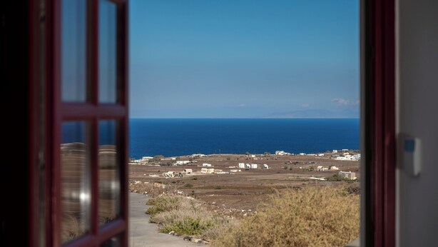 A view through an open door to a coastal area with buildings and the sea. - Zen Villas Oia  (Oia)