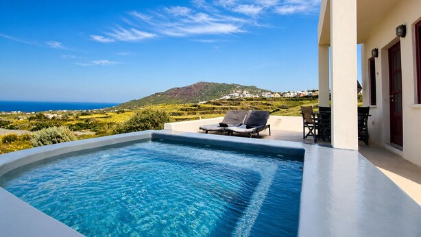 A swimming pool with lounge chairs, a view of the sea, and a hillside in the background. - Zen Villas Oia  (Oia)