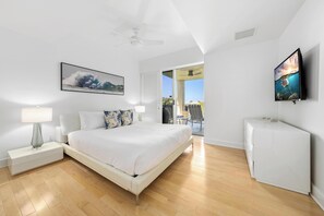 A bedroom with a bed, nightstand, lamp, ceiling fan, artwork, and a TV. - Ocean Views. C202 Vista Waikoloa (Waikoloa Beach Resort)