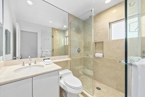 A modern bathroom with a glass-enclosed shower, a toilet, a sink, and a mirror. - Ocean Views. C202 Vista Waikoloa (Waikoloa Beach Resort)