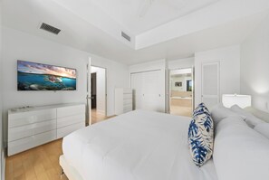 Ein Schlafzimmer mit Bett, Kommode, Fernseher und einer Tür zum Balkon.