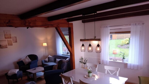 Ein gemütliches Wohnzimmer mit Esstisch, blauen Sofas und einem Holzbalken an der Decke.