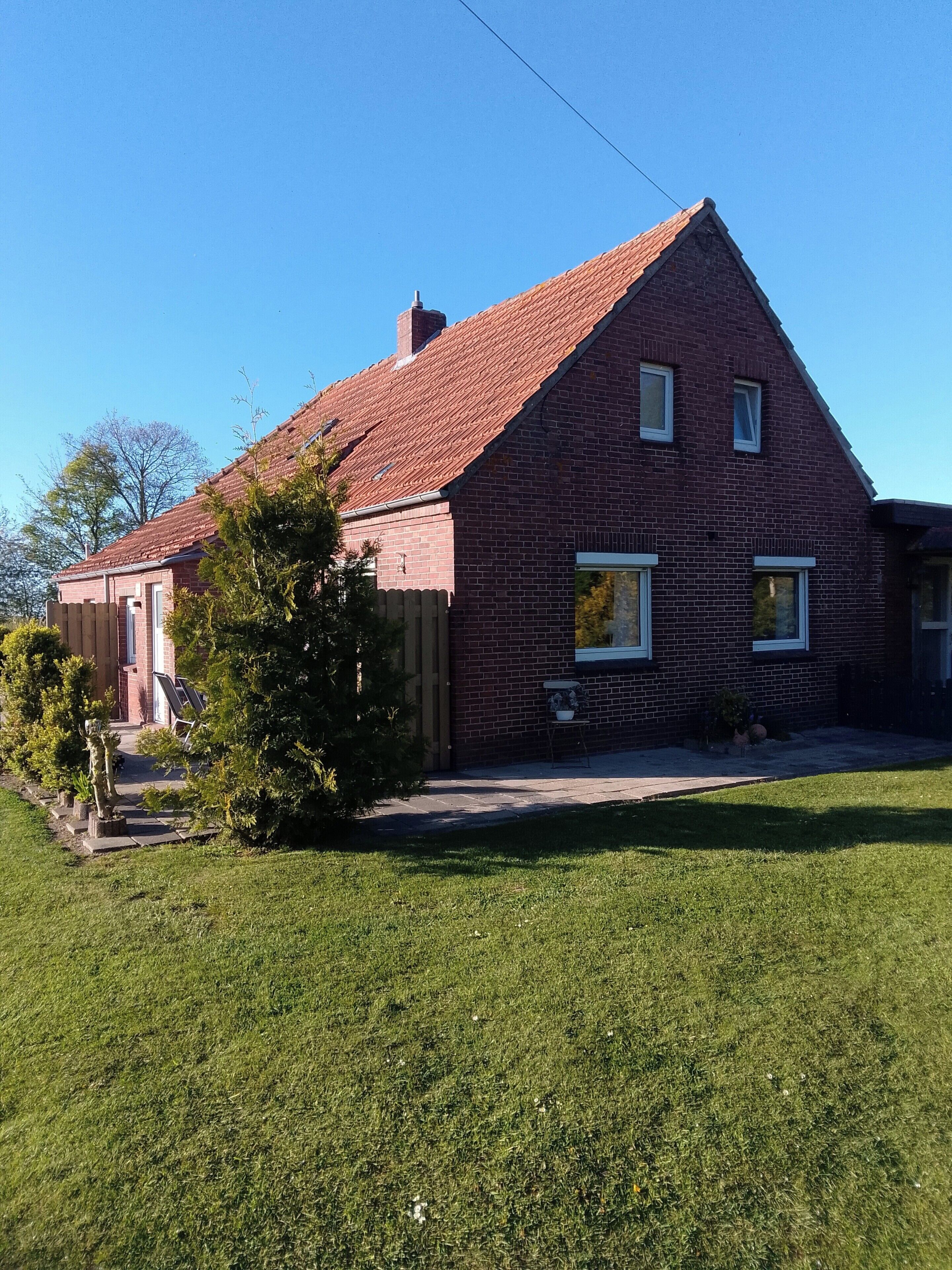 A two-story brick house with a red-tiled roof, a small porch, and a well-maintained lawn.